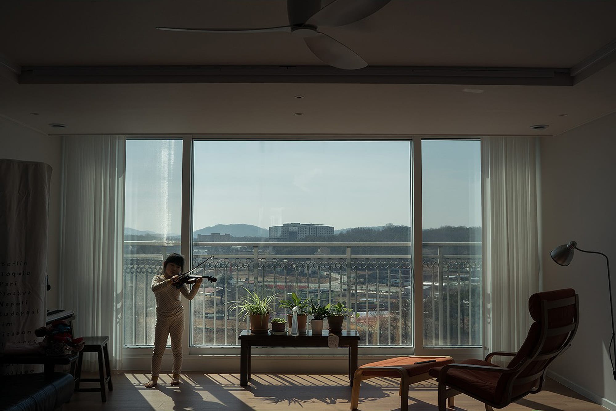 A child plays a violin in front of a window.