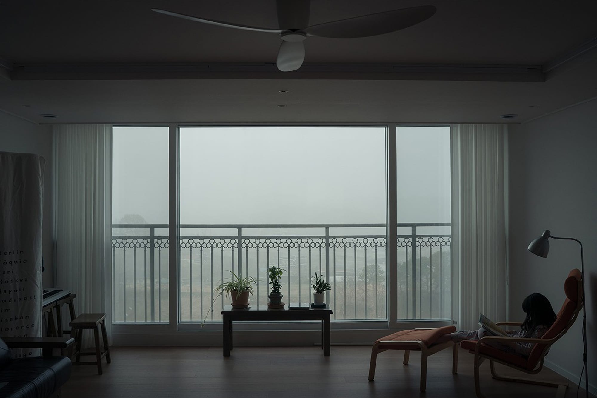 A child reads in a chair beside a cloudy window.